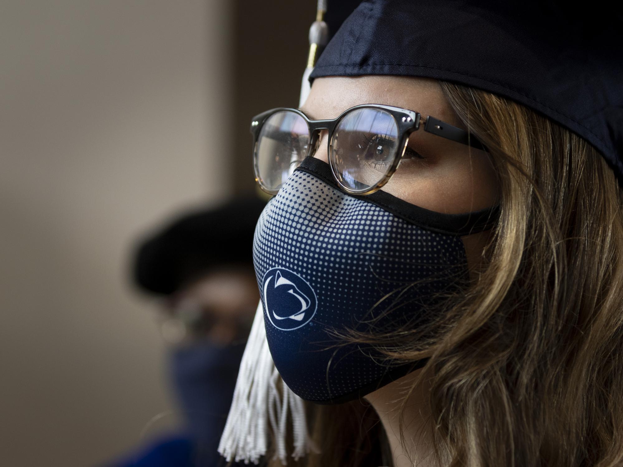 woman in glasses and mask with graduation cap on looking to the right