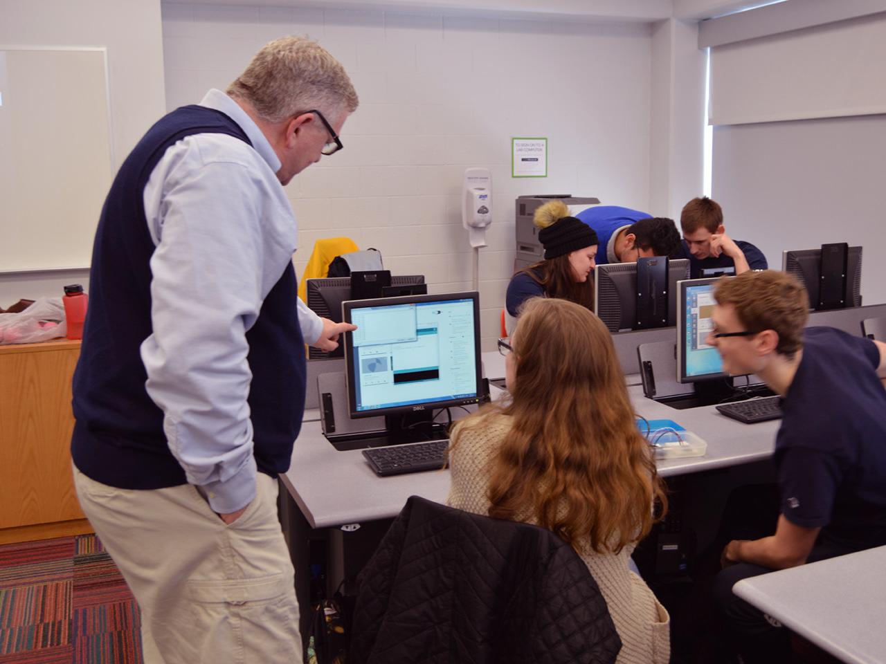 professor standing in front of student's computer pointing at screen