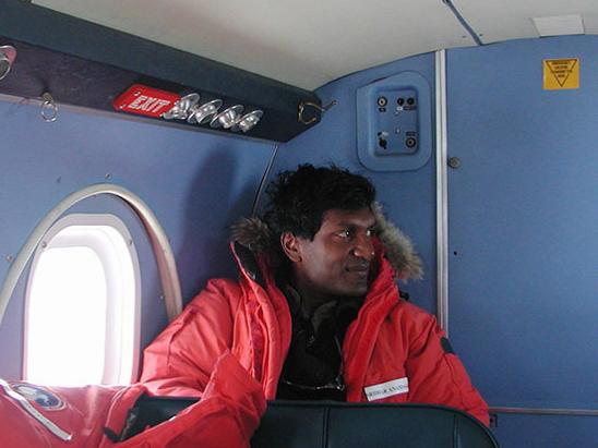A researcher in a red parka sits in a small plane with blue walls near a bright window.