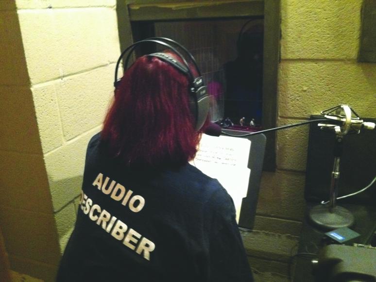 An audio describer from Sight Loss Support Group sits in a sound-proof booth and reads program notes to audience members wearing an earbud.