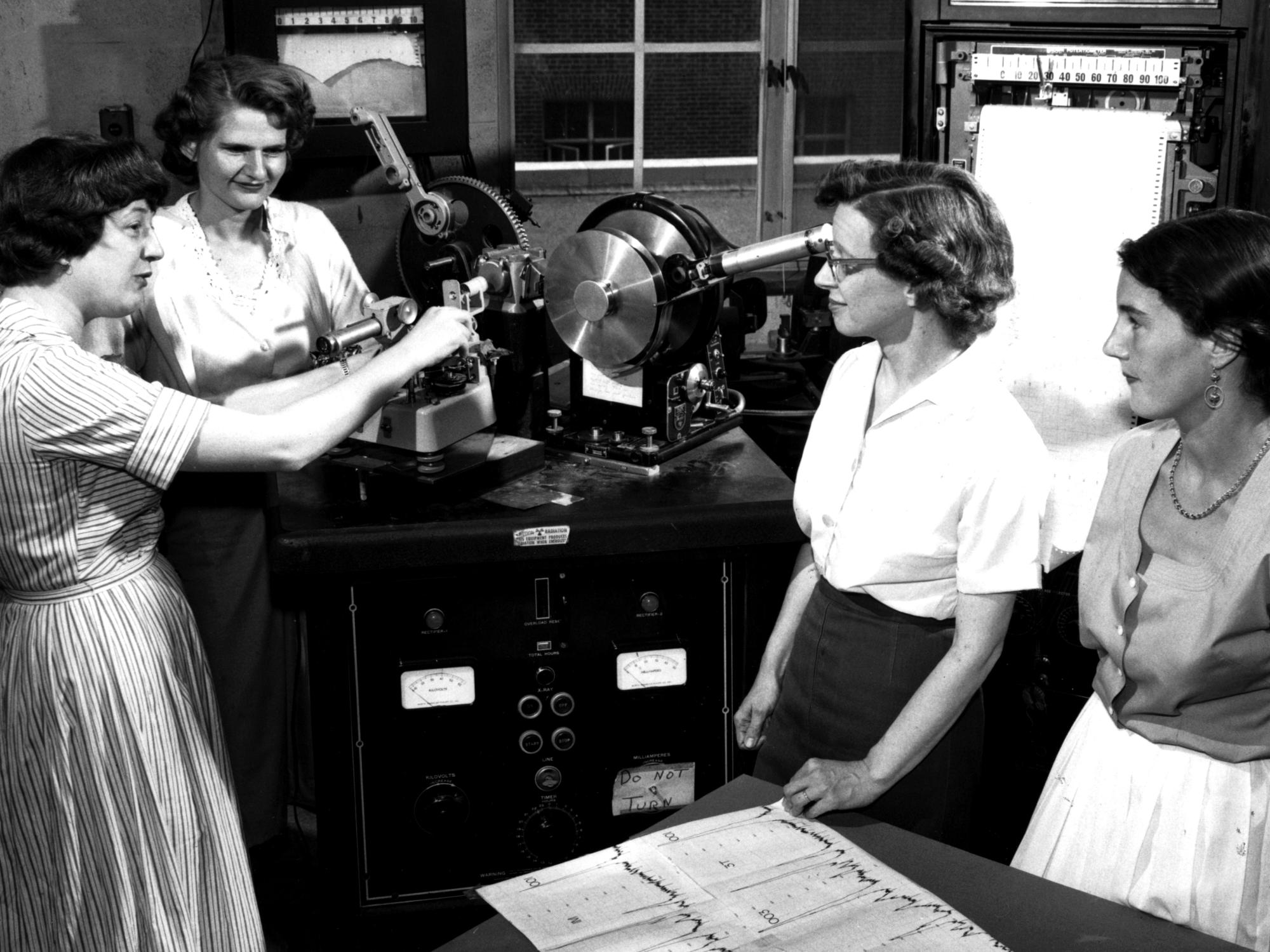 Four women in the late 50s discussing lab work.