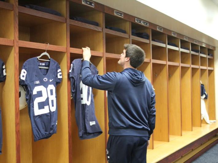 A male student, in a blue hoodie, hangs up the Penn State football jerseys. At the moment he is hanging up jersey number 40, running back Nick Eury.