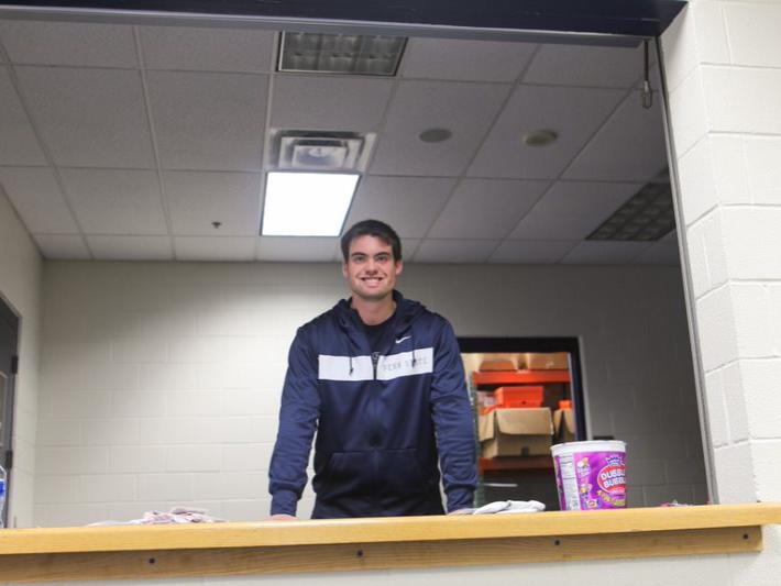 Male student leans over a counter to smile for the camera.