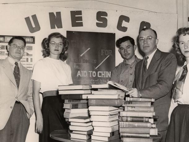 Milton Eisenhower and students stand near a table of books under a sign reading "UNESCO."