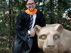 Person wearing master's degree commencement robes leans against Nittany Lion Shrine