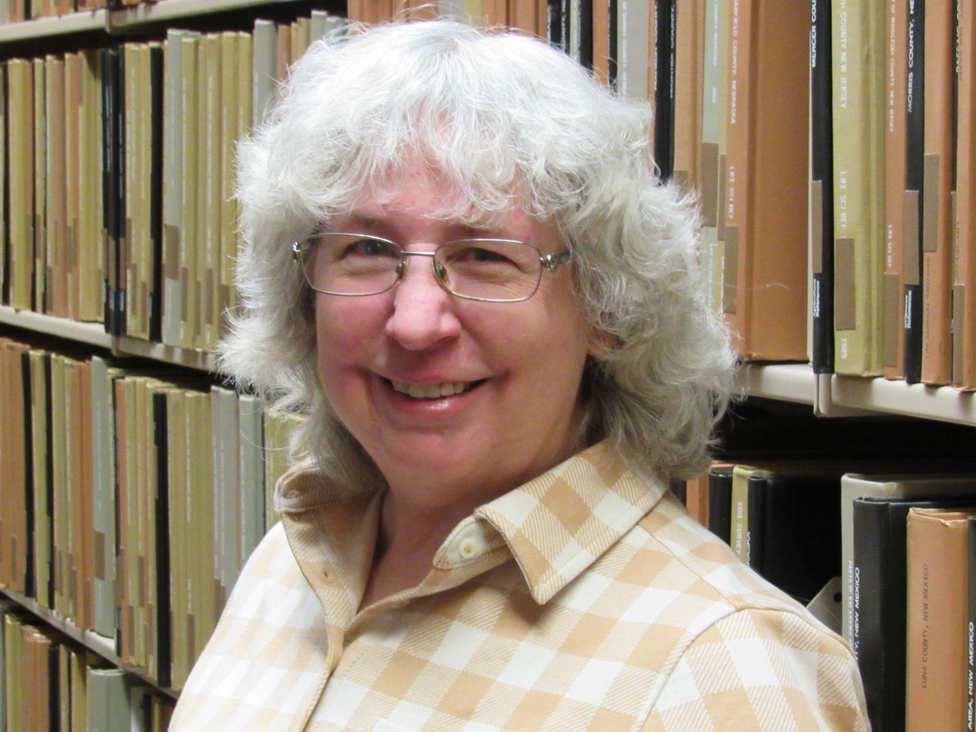 standing woman smiling at camera in front of shelves of books