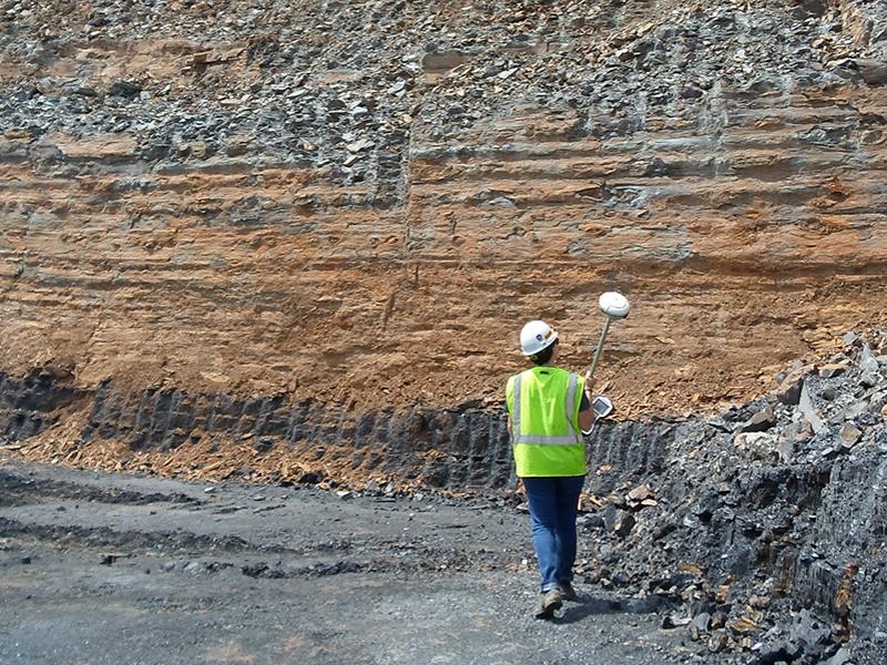 student holding surveying equipment at surface mine