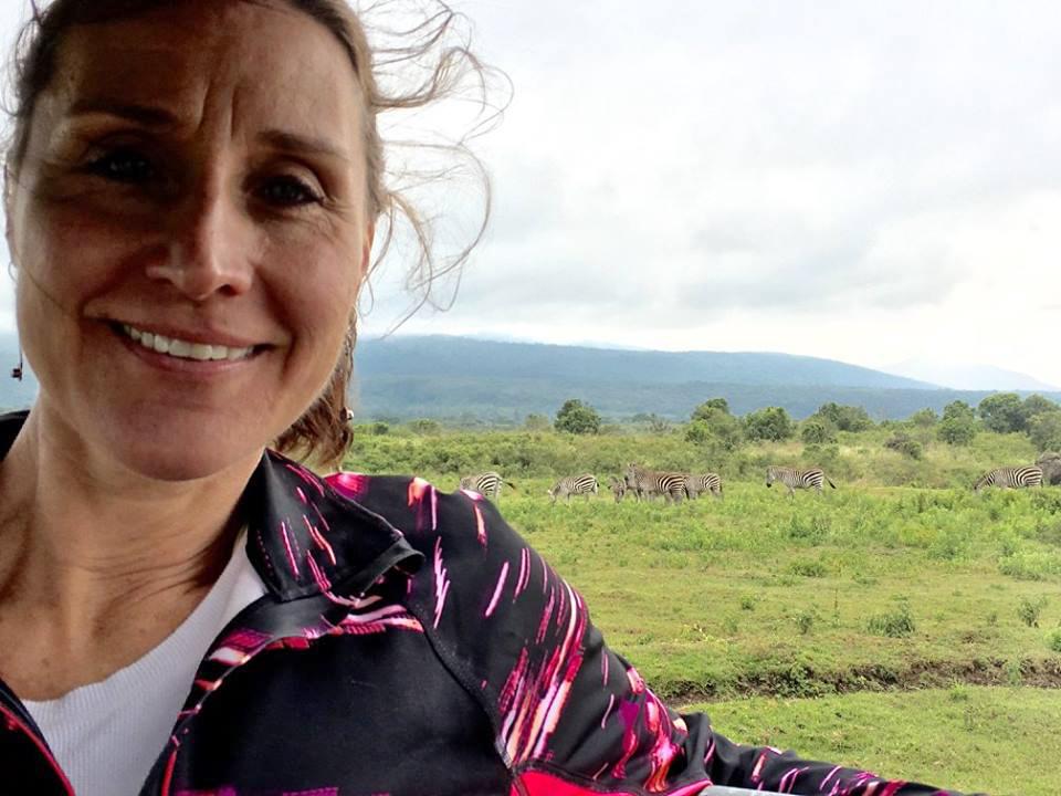 woman in foreground with zebras pictured behind her