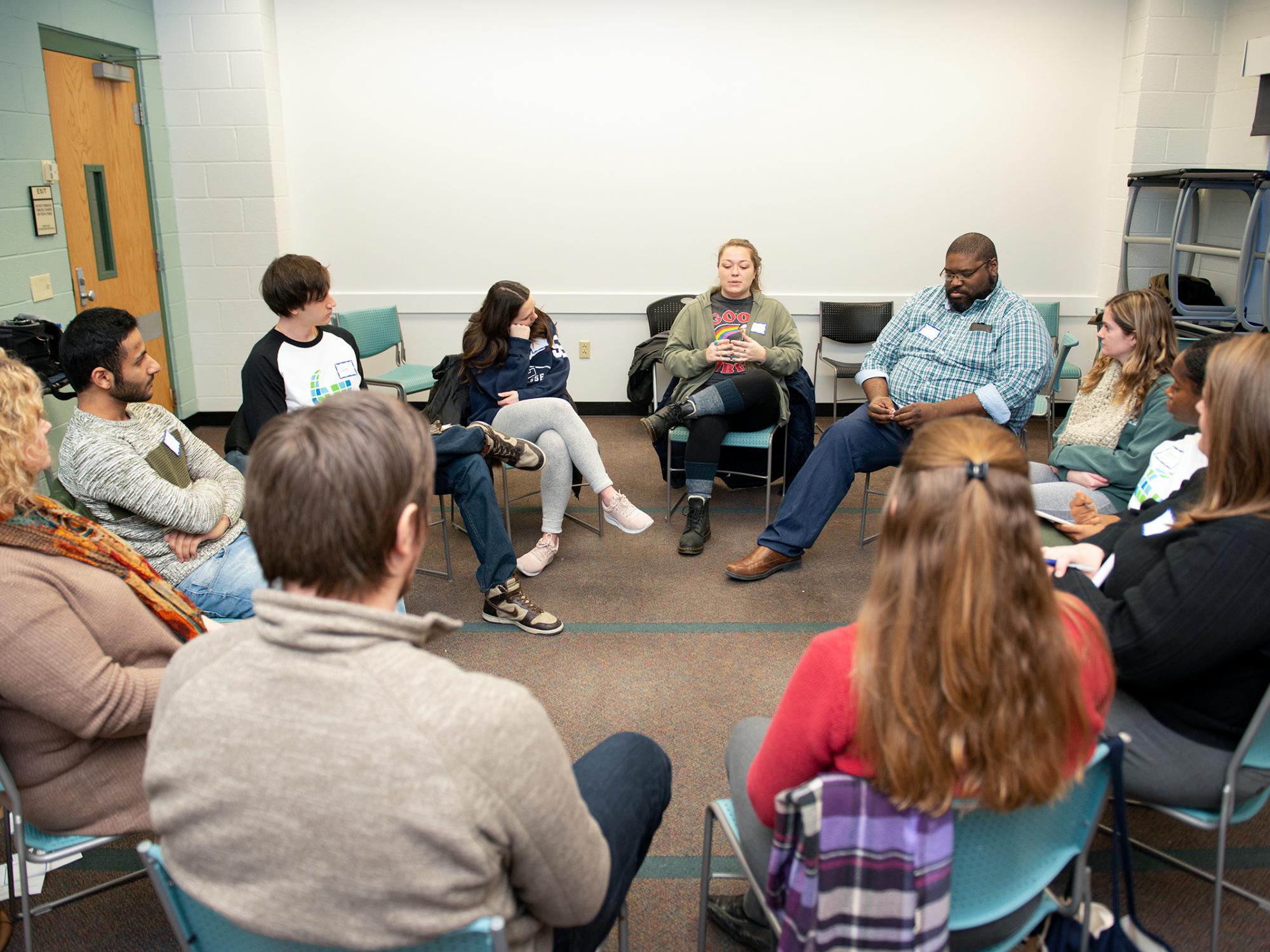 A group of people sit in a circle to have a facilitated conversation.