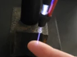 A laser-like jet is projected onto the underside of an index finger.