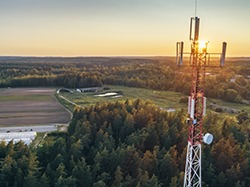 Sunlight pours through a broadcasting tower that overlooks green open area with trees