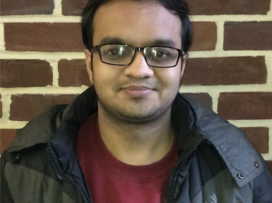 male student in t-shirt and jacket posed in front of brick wall 