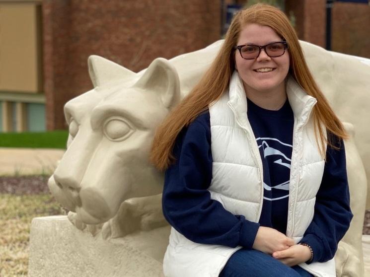 Female student sits next to lion shrine statue
