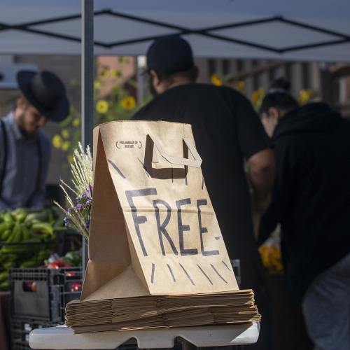 A paper bag labeled "Free Food" sits in front of a stall of fresh produce