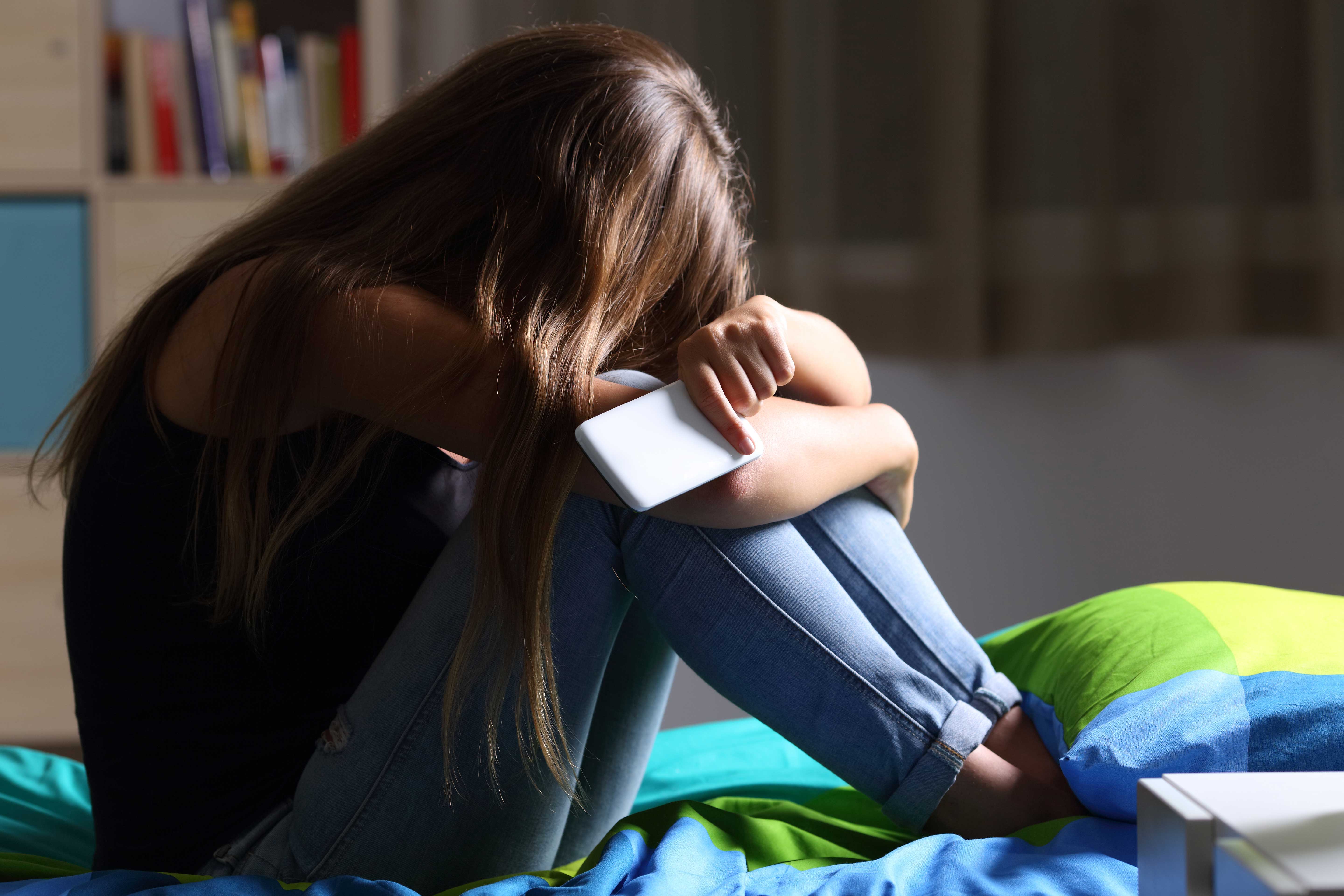 Teen seated on bed, cradling their knees