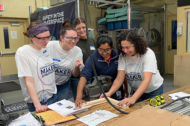 Four women stand around a table covered in wood pieces and power tools. 