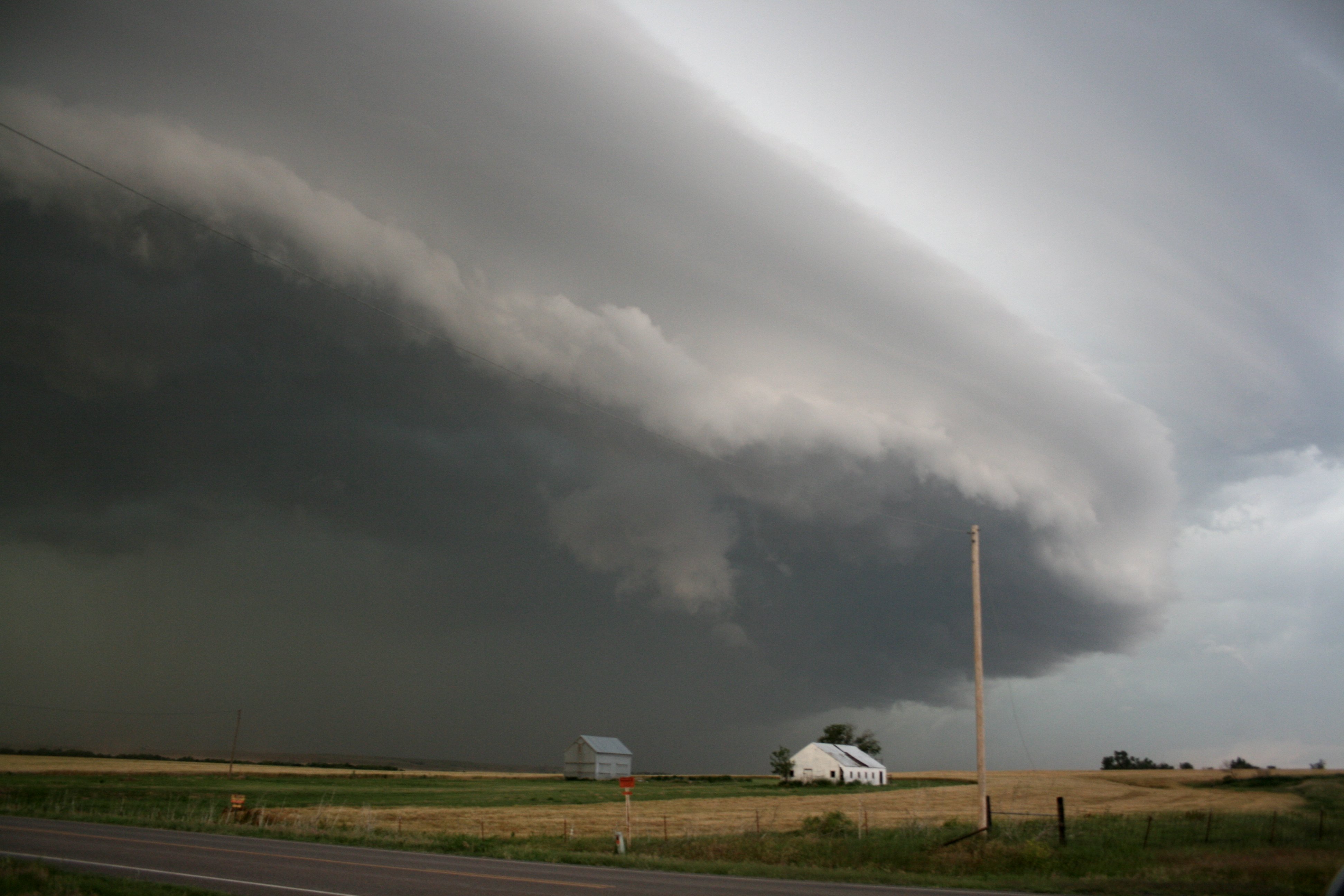 A large storm cloud over a farmhouse and flat fields