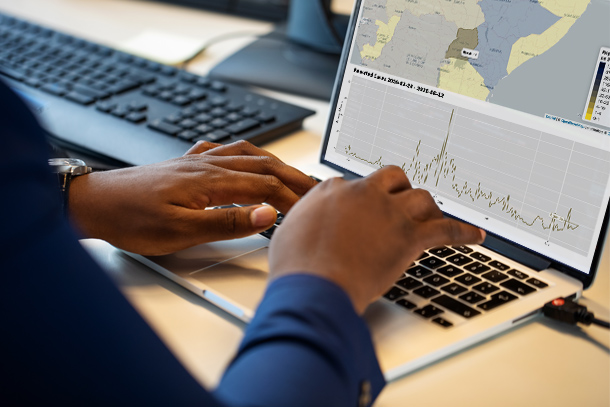 Black hands types on a laptop, displaying data about COVID-19 cases in Uganda.