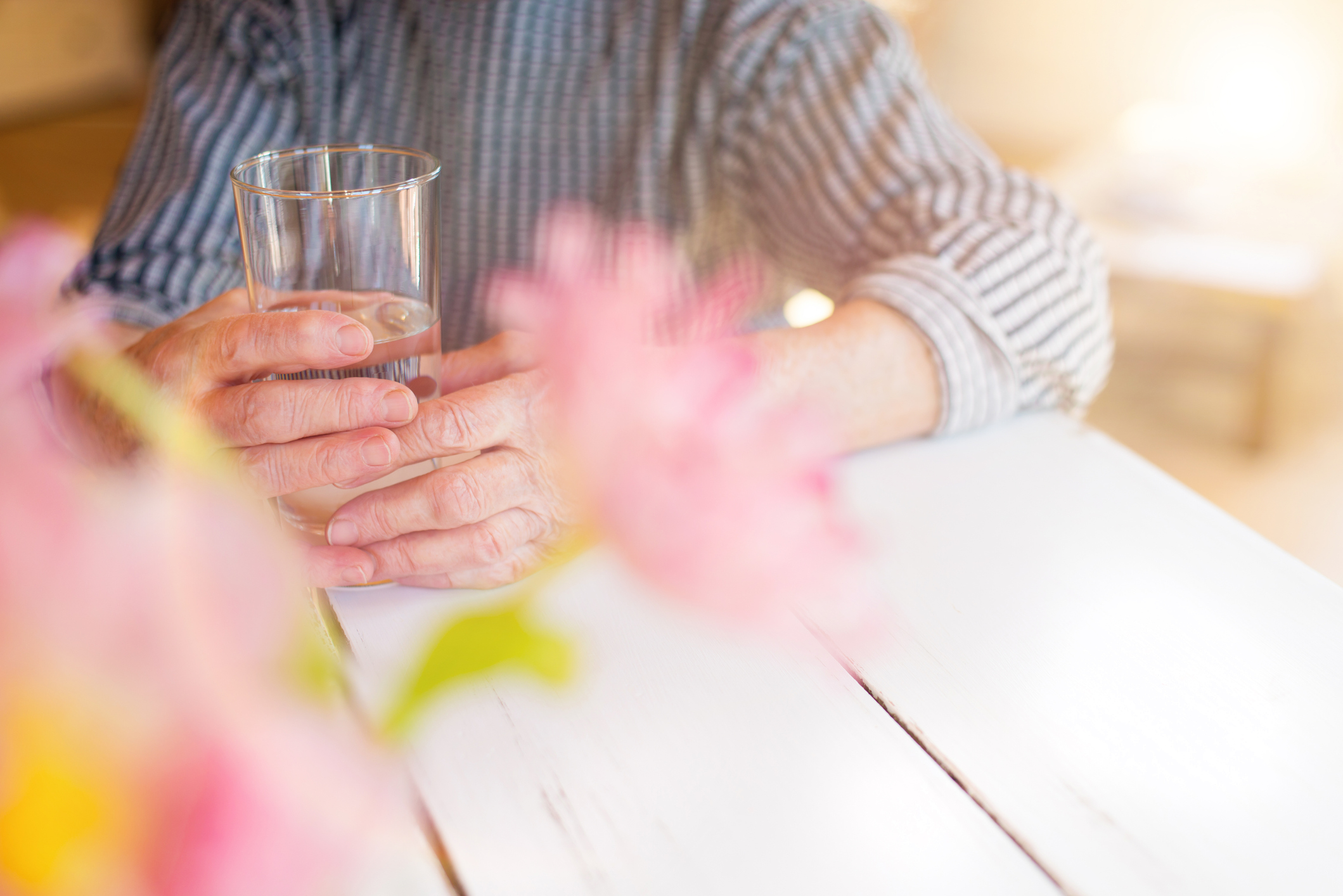 Close up photo of an older person's hands holding a glass of water