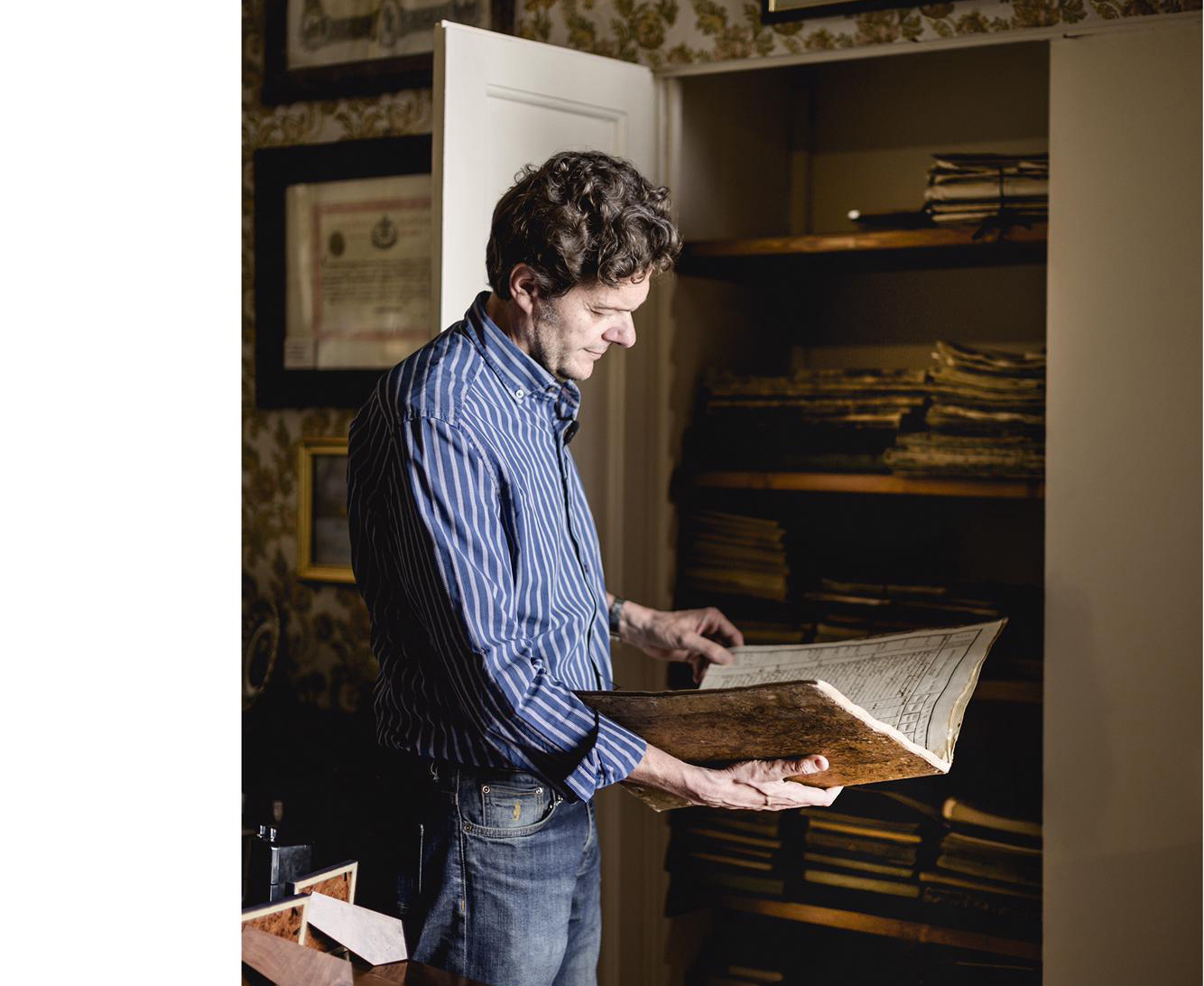 Man holding an old ledger listing grape production in front of a closet containing 200 years worth of ledgers